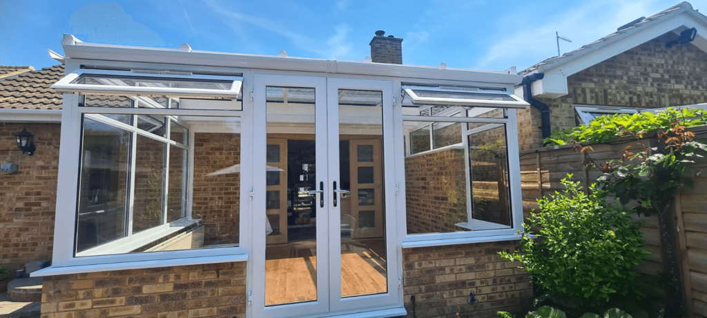 White uPVC conservatory with double-glazed French doors and opening windows, installed on a brick base for a modern home extension.